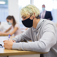 male teenager sitting in class with mask